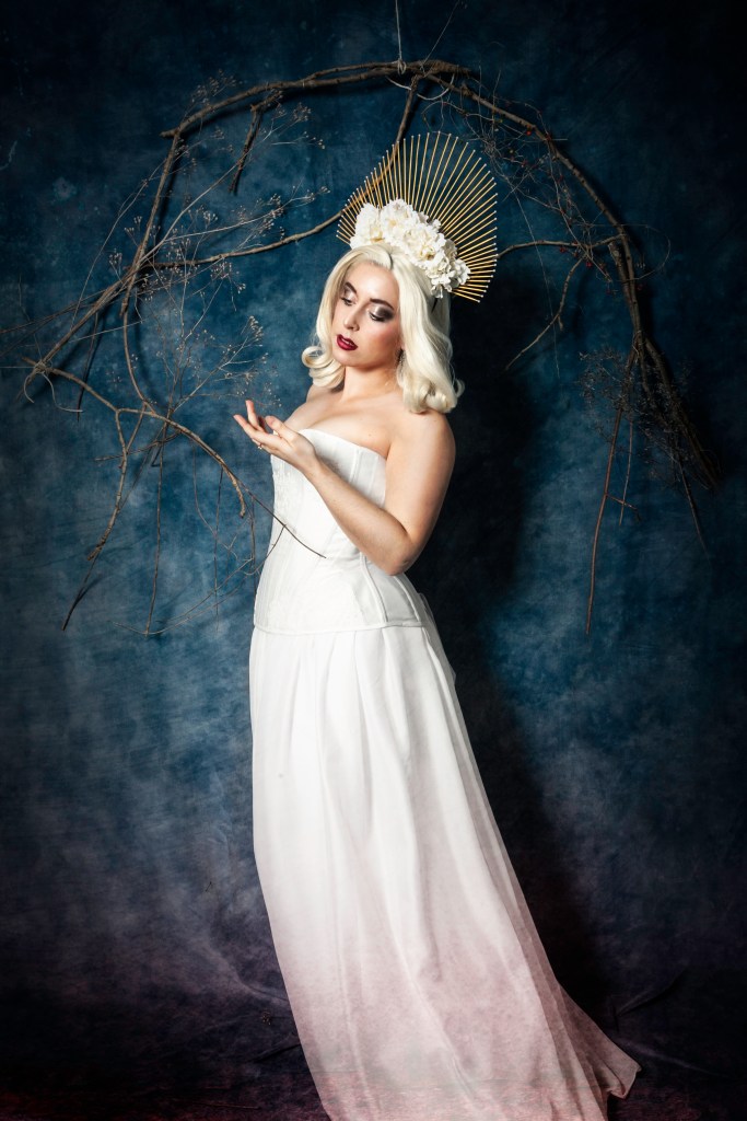 Corset blanc et dentelle, coiffe dorée, fleurs et perles blanches.