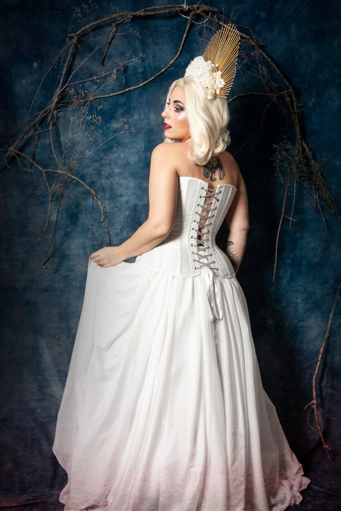 Corset blanc et dentelle, coiffe dorée, fleurs et perles blanches.