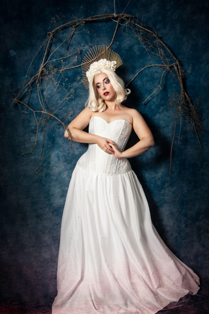 Corset blanc et dentelle, coiffe dorée, fleurs et perles blanches.